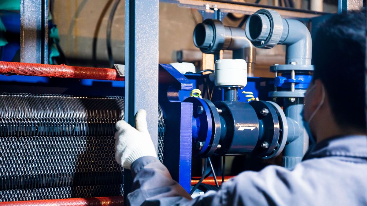 Tecnico al lavoro su una centrale tecnologica con valvole e scambiatore di calore